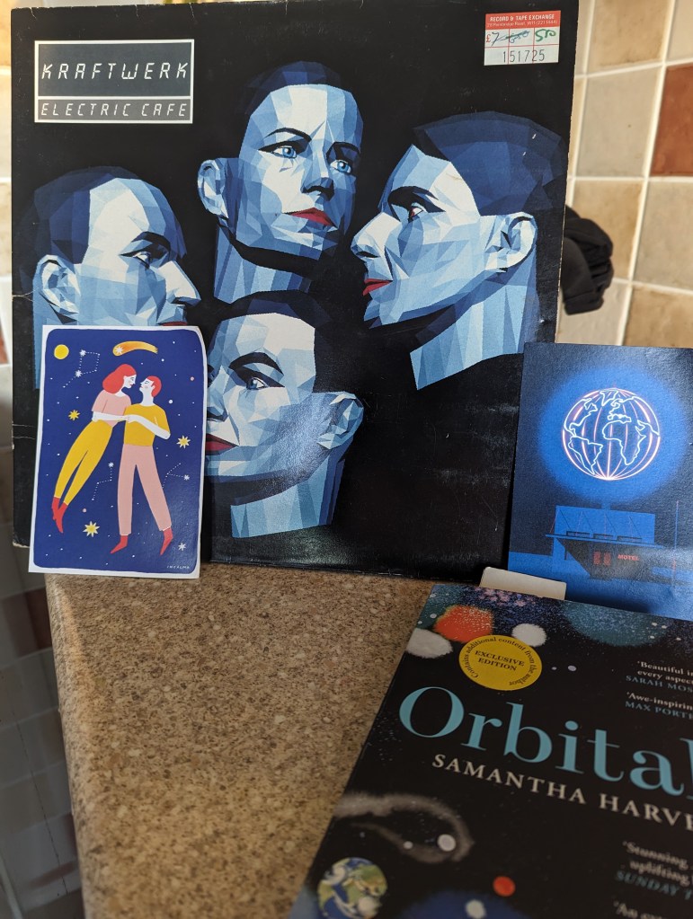 Album cover of Kraftwerk album Electric Cafe and a copy of Orbital by Samantha Harvey